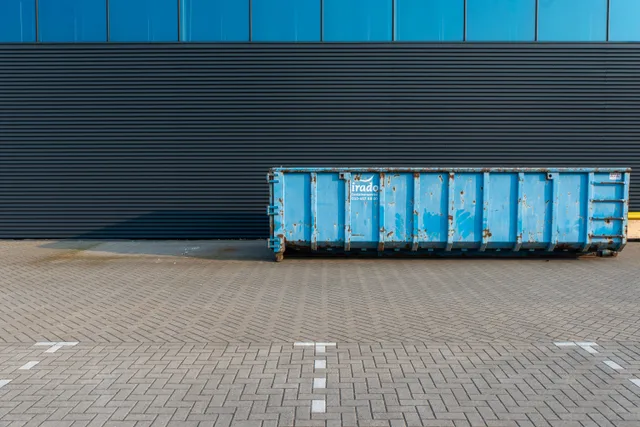 A blue industrial dumpster placed beside a modern building facade, featuring clean lines and urban setting. Dumpster rental suppliers in plain terms