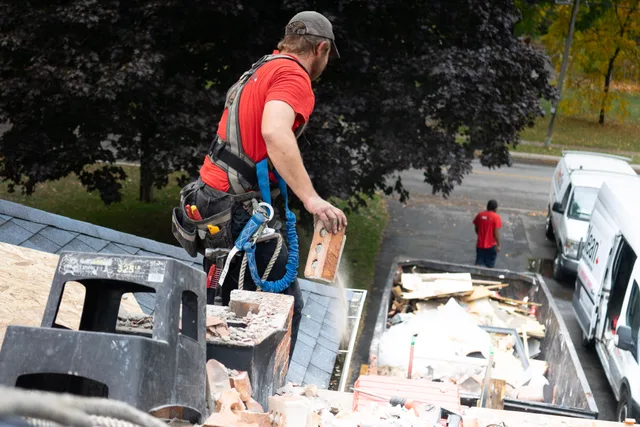 Worker in safety harness removes bricks from roof into dumpster below. How National and Regional Dumpster Companies Compete