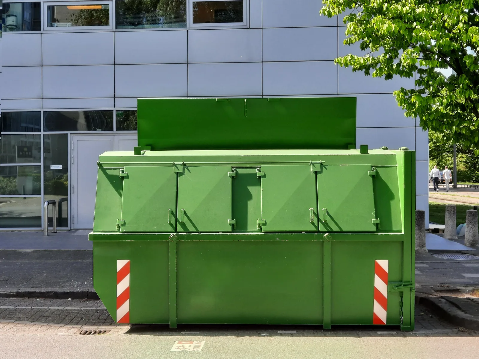 A green dumpster is placed outside an urban building in Den Haag. Dumpster rental business plan: the parts people skip