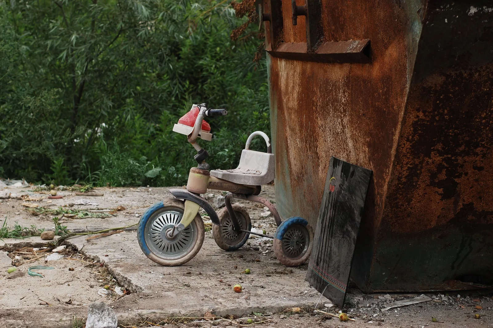 A forgotten tricycle rests next to a rusty dumpster among overgrown greenery in Kaliningrad. Dumpster rental downtime: what it actually costs per idle day