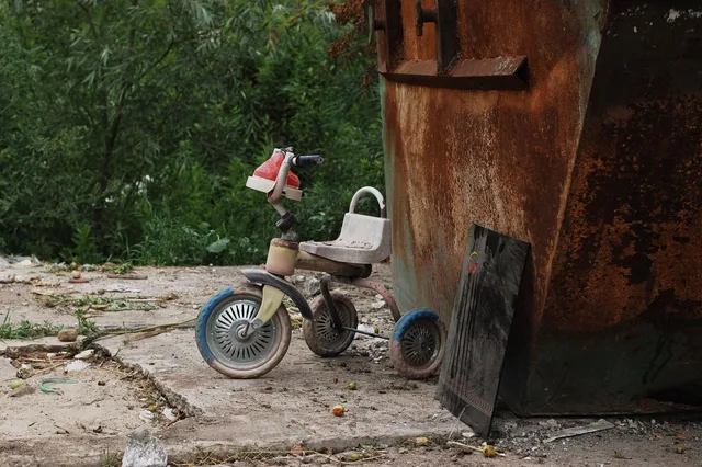 A forgotten tricycle rests next to a rusty dumpster among overgrown greenery in Kaliningrad. Dumpster rental downtime: what it actually costs per idle day