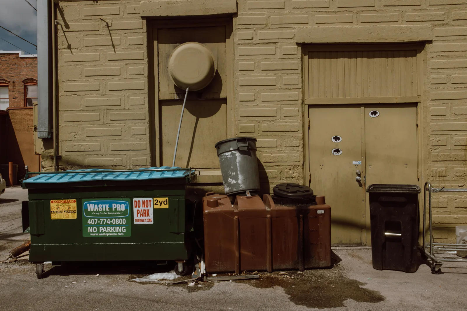 Sunlit alleyway featuring trash bins and dumpsters beside a textured urban wall. Writing dumpster rental quotes: a template plus priced examples