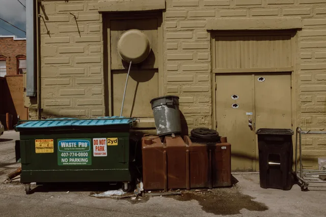 Sunlit alleyway featuring trash bins and dumpsters beside a textured urban wall. Writing dumpster rental quotes: a template plus priced examples